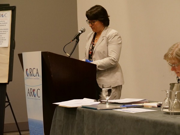 A speaker stands at a podium, which has the bilingual ORCA logo on the front. 