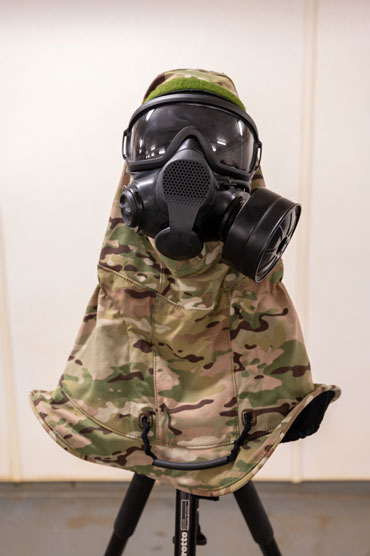A respirator with an attached hood is set on a tripod. The hood has a camouflage print.