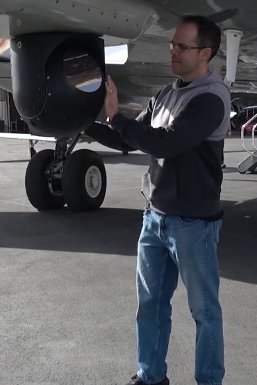 Une personne en tenue civile ajuste une sphère avec une lentille réfléchissante montée sous un avion.