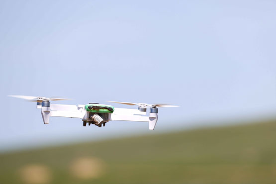 A quad-copter drone with burn marks on the main body is flying.