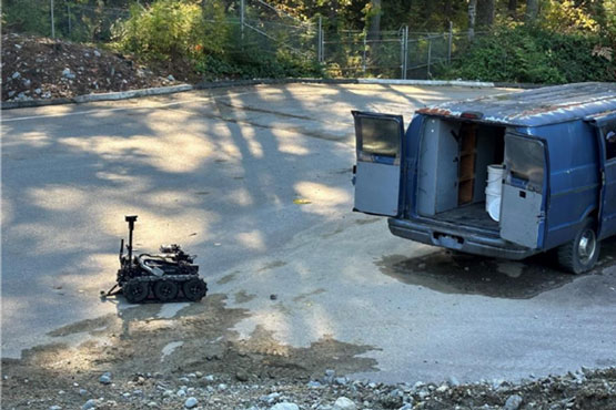 A robot on the ground beside an open van.