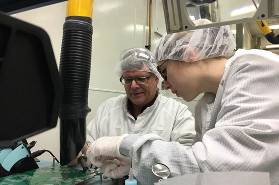 Two people in lab coats and hair nets work in a laboratory.