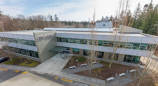 A building seen from outside, with a large sign with the acronym NRC-CNRC. The building has trees and benches by the entrance.