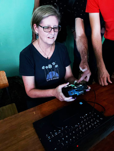 A woman seated at a table holds a joystick controller plugged into a laptop computer.