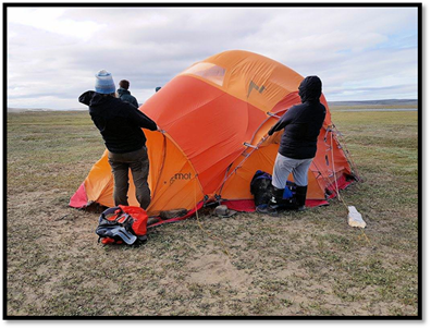 Allison and another team member holding up the cooking tent against the 30-40 km/h winds while other team members fix a snapped pol on the other side. Photo by Sally Esau of Parks Canada