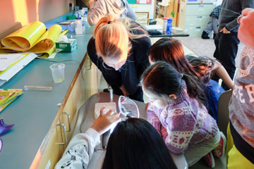 Une chercheuse scientifique et trois enfants d’âge scolaire se réunissent autour d’un microscope.