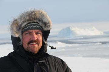Research scientist wearing a parka smiles at the camera against a snowy background.