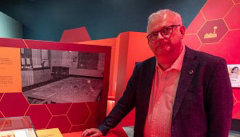 Que le meilleur gagne! Les analystes de RDDC prennent les jeux de guerre au sérieux / Un homme regarde une photo en noir et blanc exposée dans un musée sous une lumière rouge et sur laquelle on voit une table de jeu de guerre.