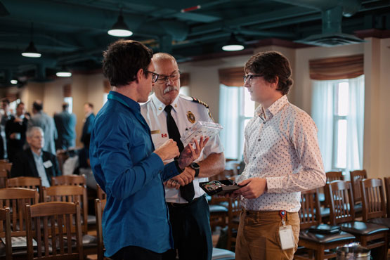 A person in an Ottawa Fire Services uniform discusses technology prototypes with two researchers.