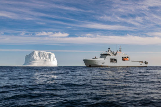 A grey Royal Canadian Navy ship, the HMCS Harry DeWolf, is shown with an iceberg.